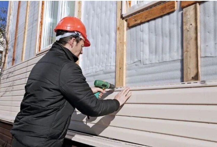 Construction worker installing siding with a power drill on a building exterior.