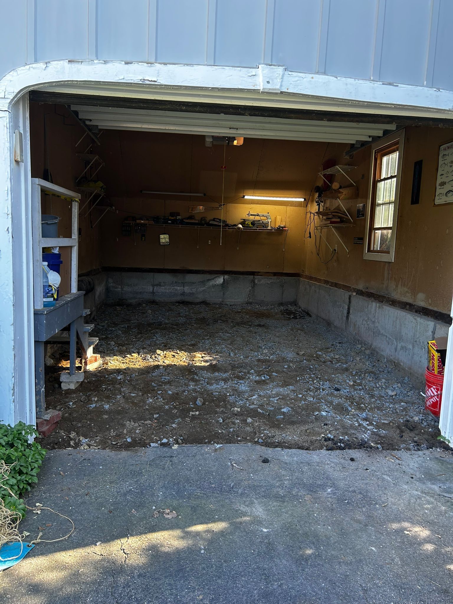 Open garage with a dirt floor, tools, and a window.