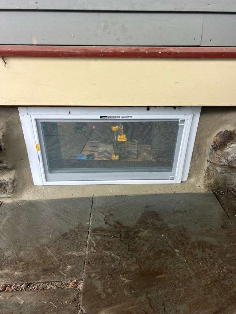 Basement window with a white frame and screen set in a stone wall.