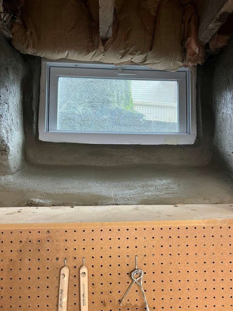 Basement window in a concrete wall with pegboard below.