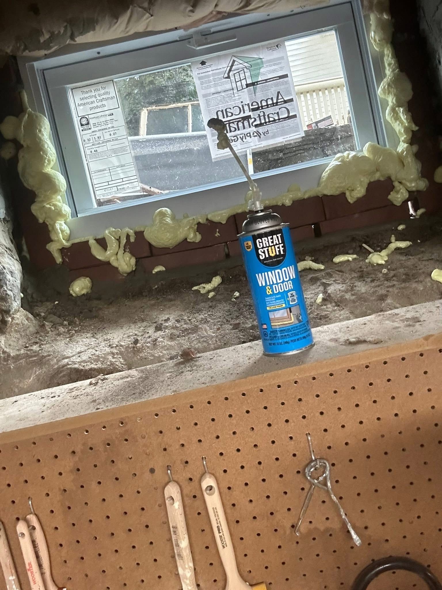 Window being sealed with spray foam; blue can, white window frame, brick wall.