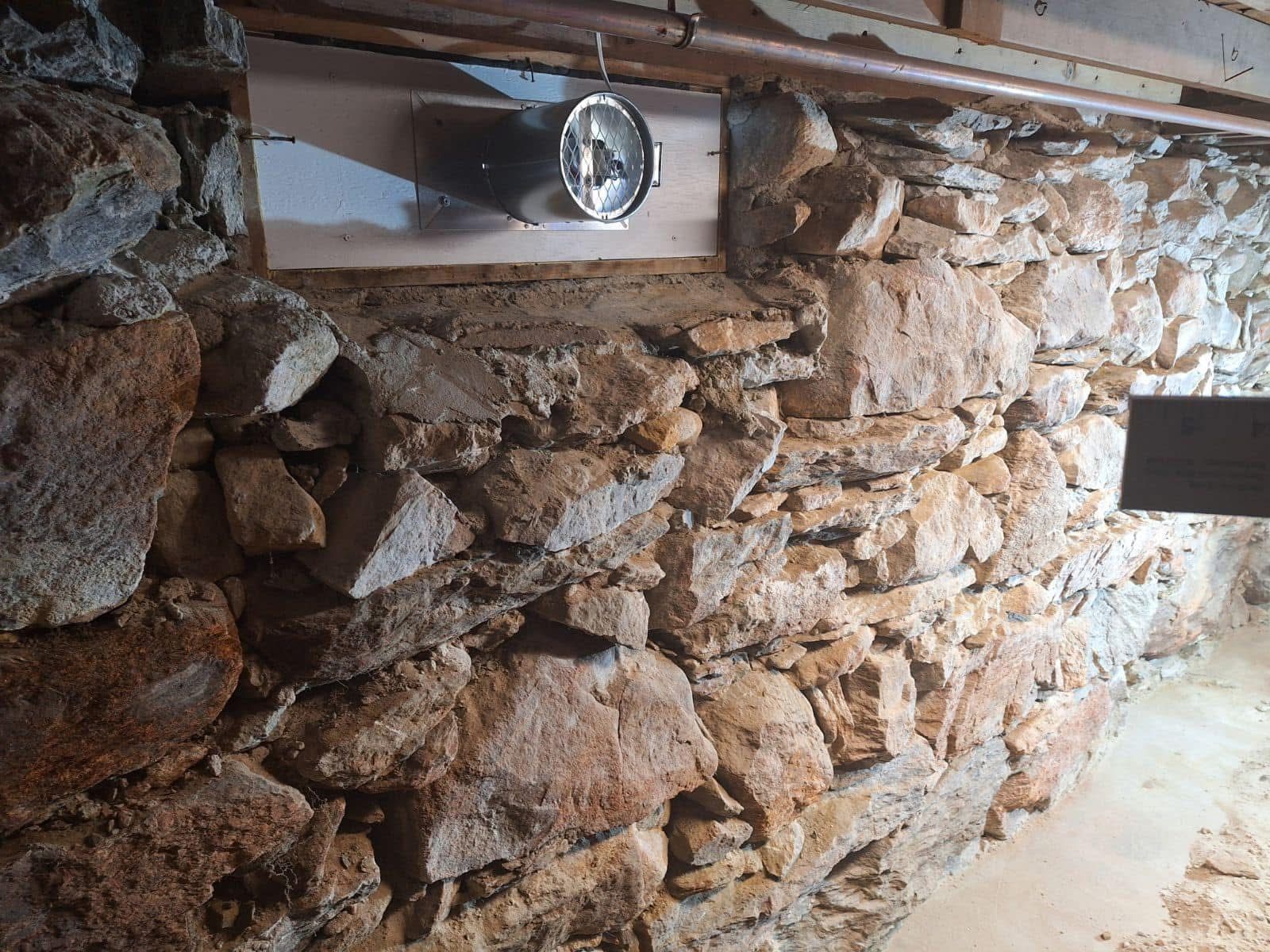 Stone foundation wall with a pipe and metal fixture attached to it.