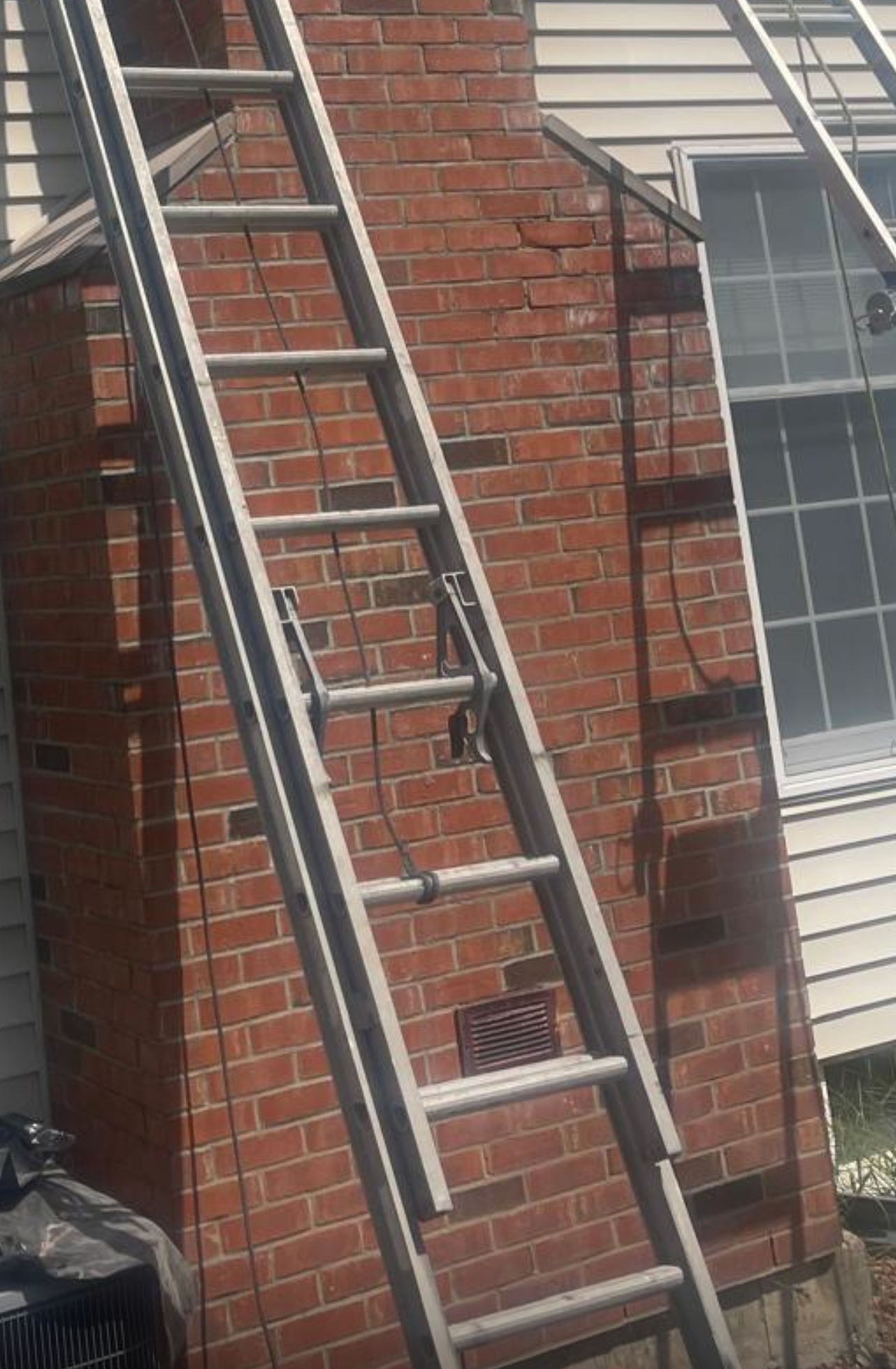 Ladder leaning against a brick chimney next to a house with a window.