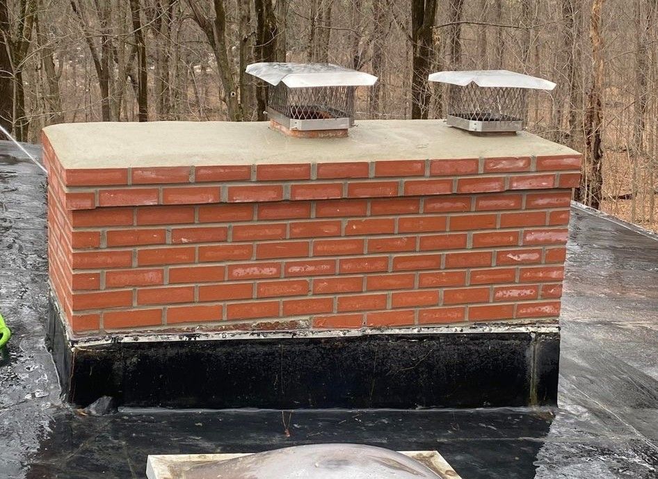 Brick chimney on a black flat roof with two metal chimney caps.