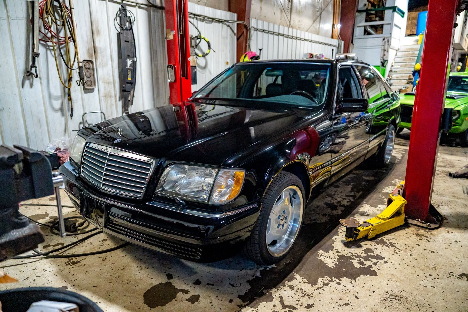 Black Mercedes sedan in a garage, parked near a car lift and tools.