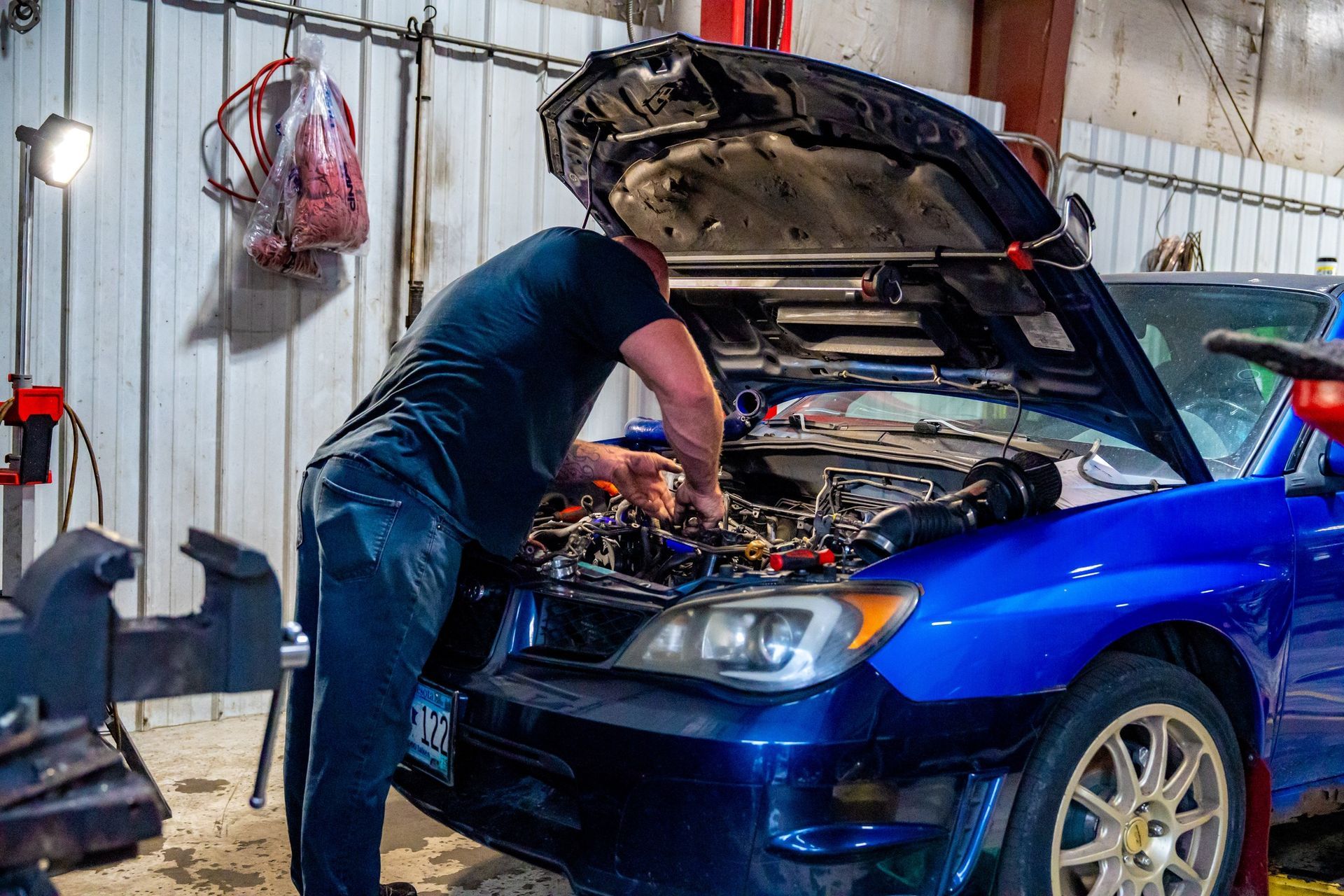A mechanic working on a blue car with the hood open in a garage.