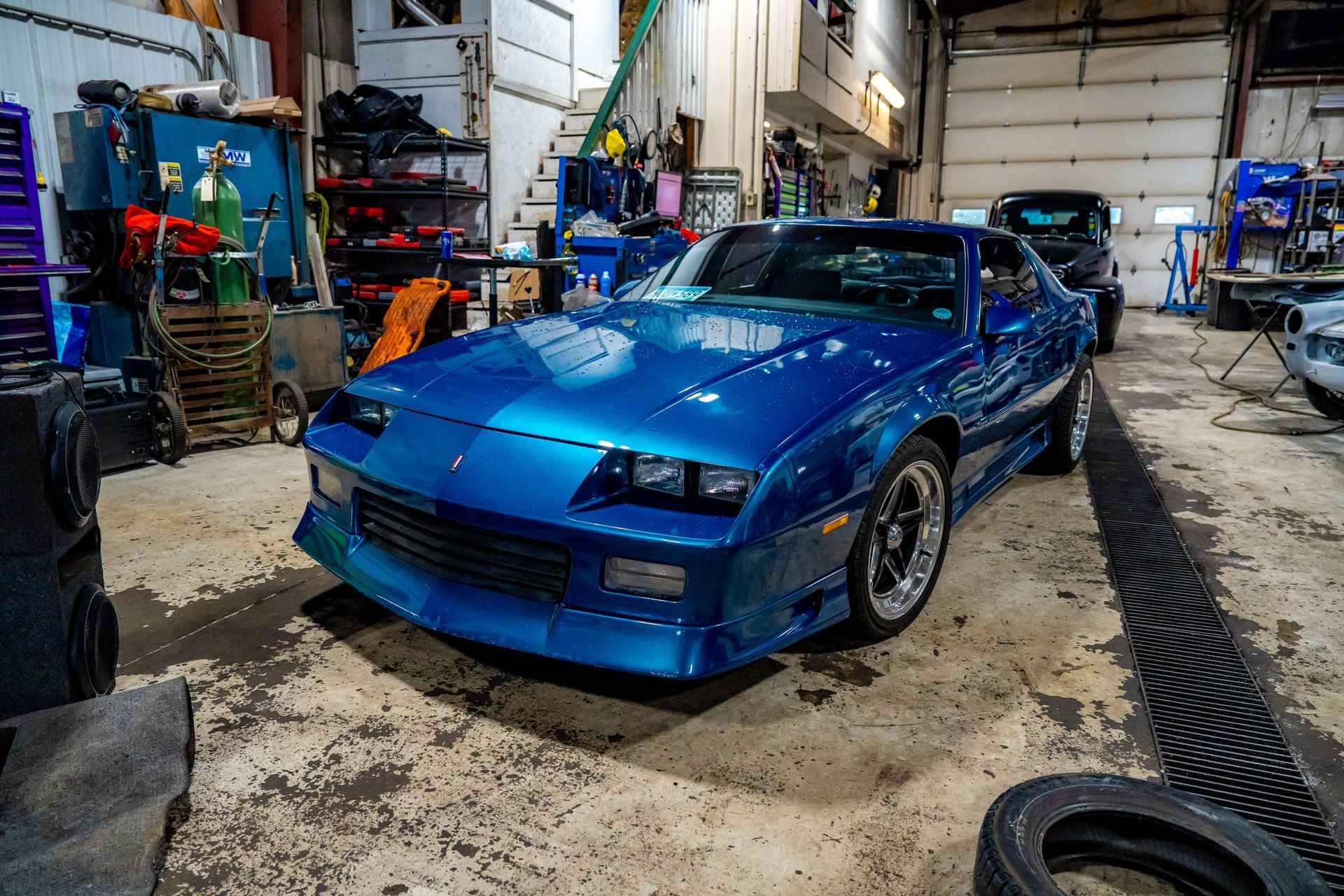 Blue Chevrolet Camaro in a cluttered garage with tools.