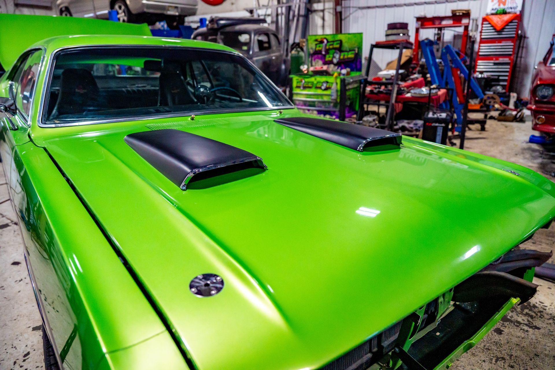 Bright green muscle car hood with black vents in a workshop.