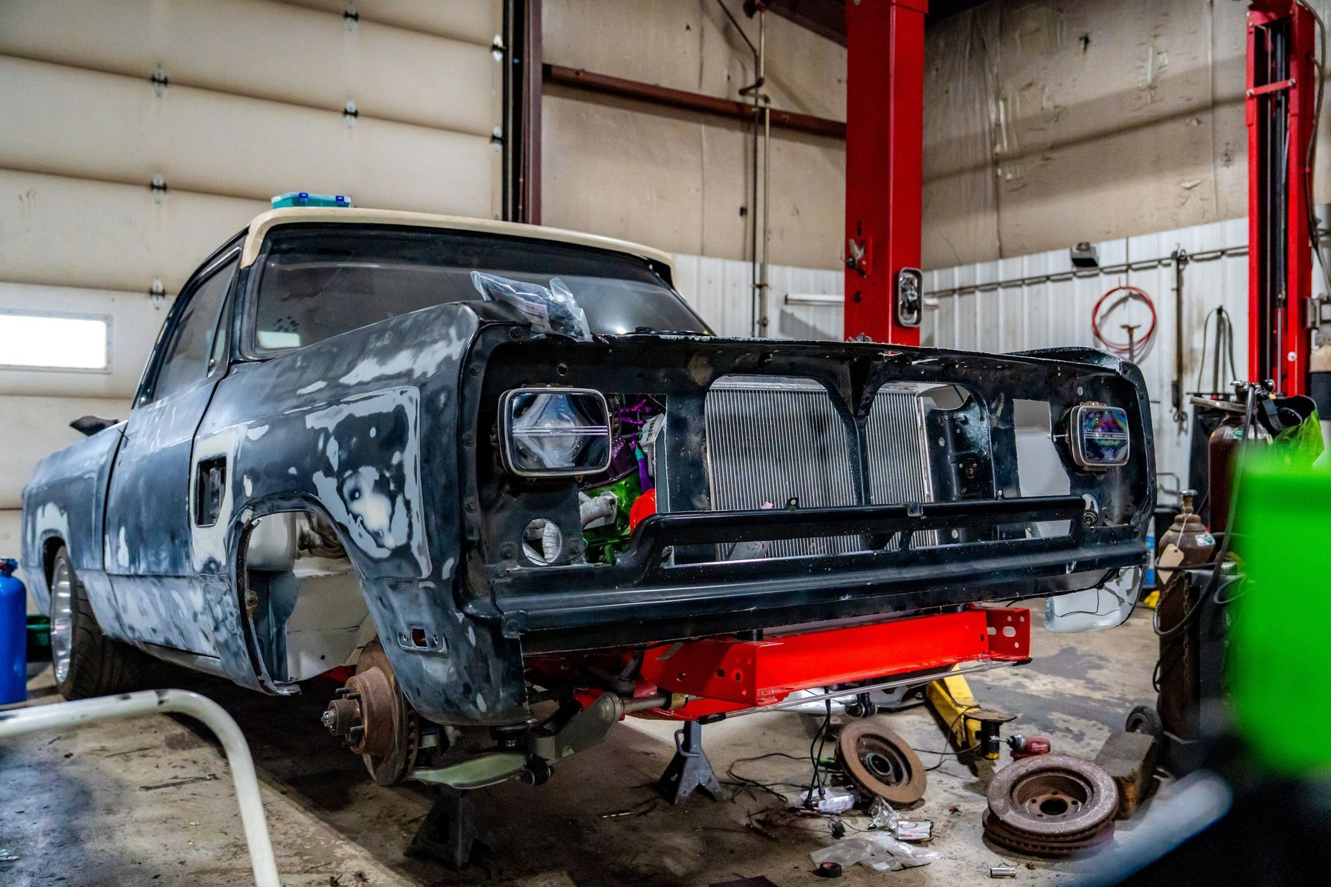 Truck cab in a workshop, undergoing restoration. Body panels removed, front end painted red.
