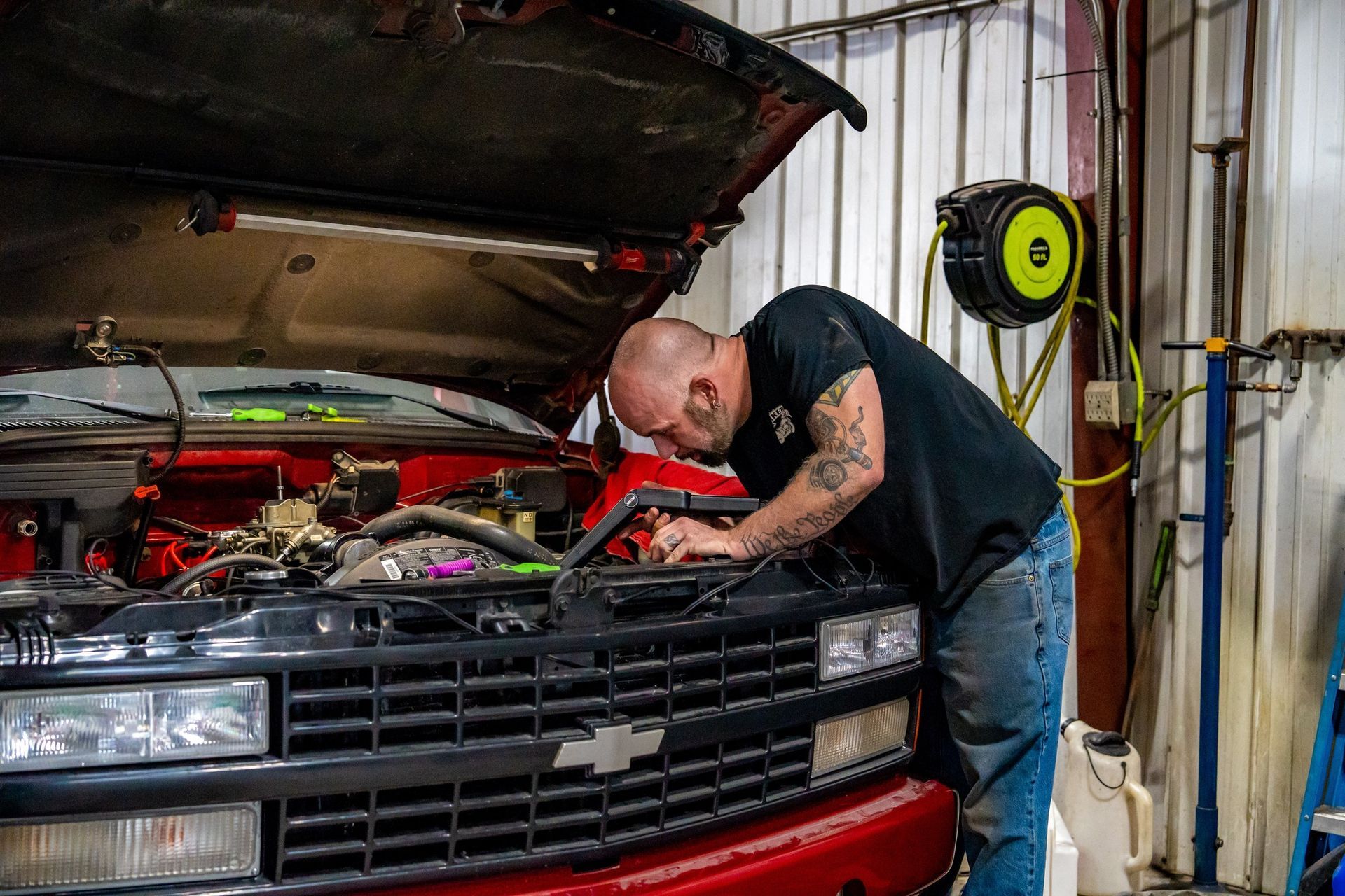 Man with tattoos works on the engine of a red Chevrolet truck in a garage.