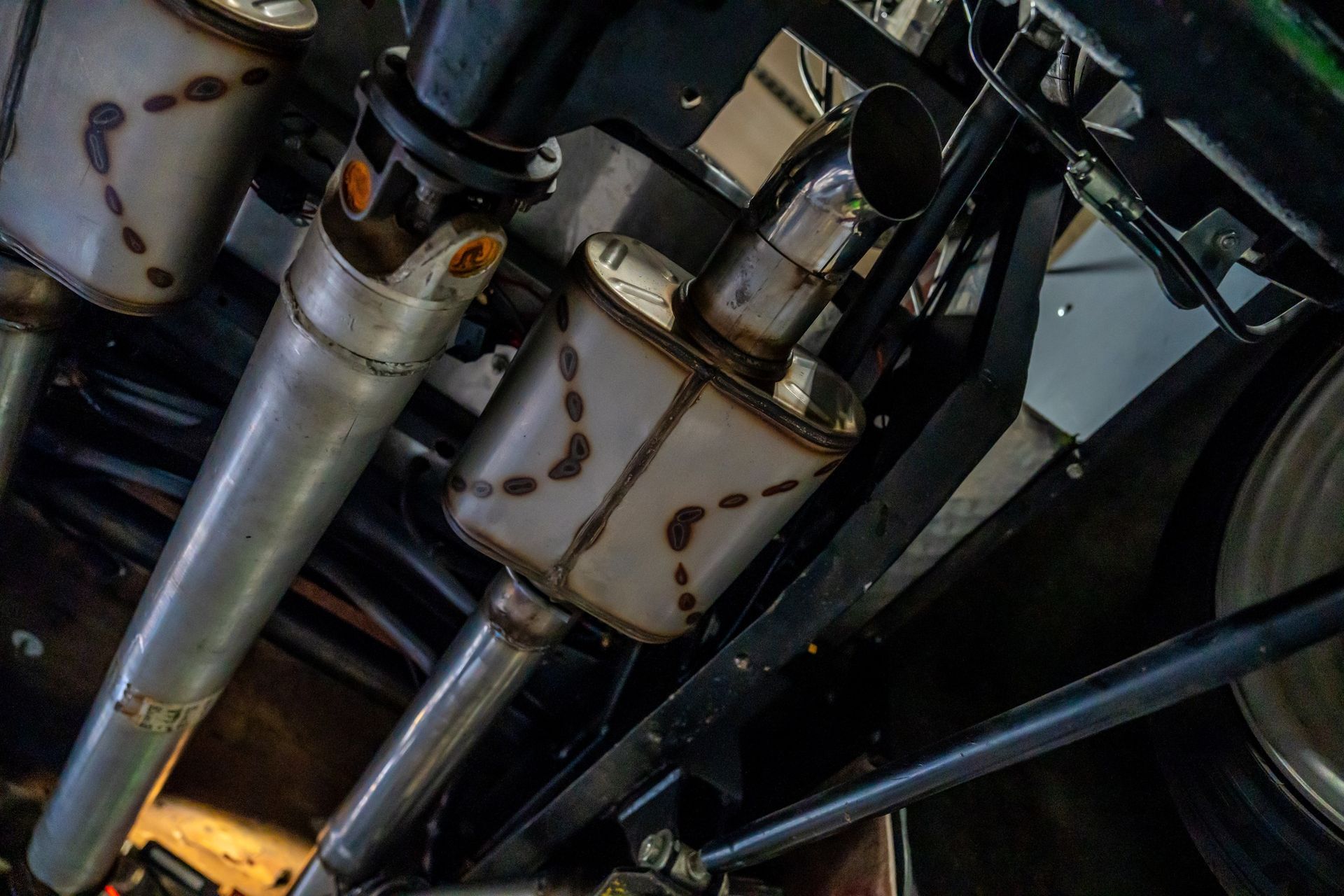 Undercarriage view of exhaust system with mufflers, silver pipes, and welding marks.
