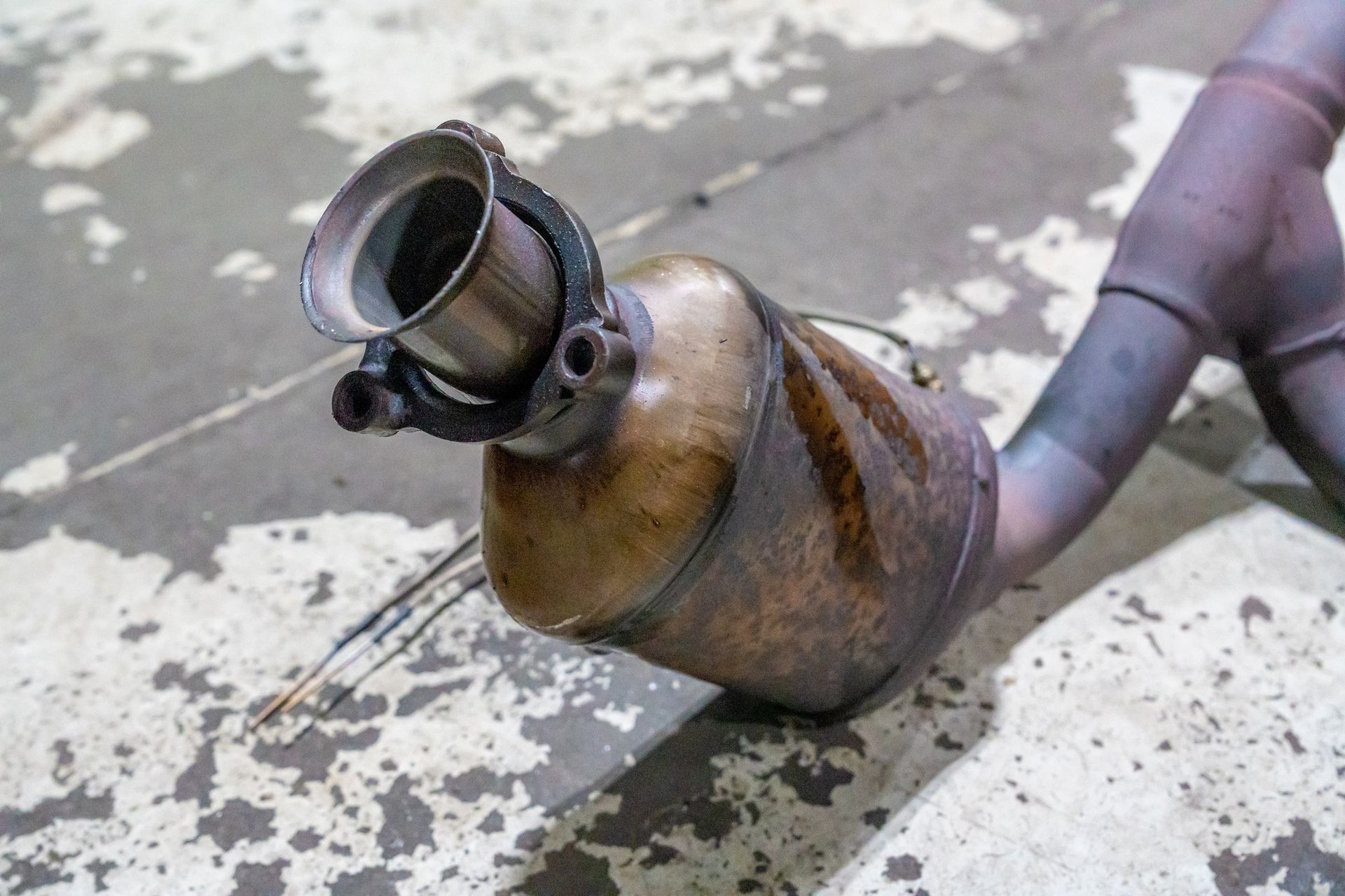 A rusty catalytic converter with a cut-off pipe, showing internal structure, on a light-colored surface.