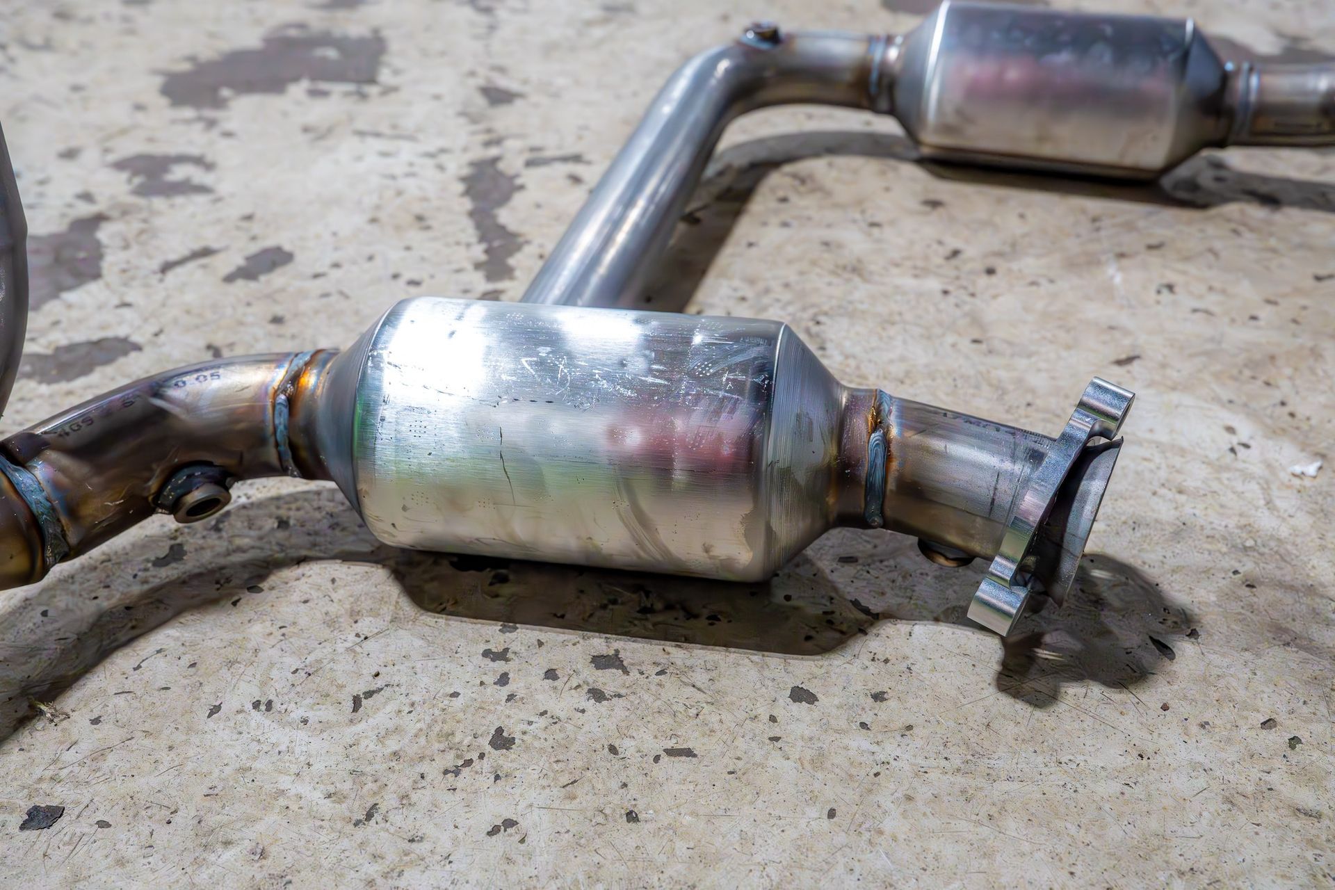 Silver catalytic converter with flanges and welded pipes on a concrete surface.