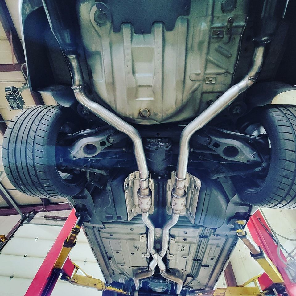 Underneath view of a car on a lift with a new dual exhaust system, with shiny silver pipes and mufflers.