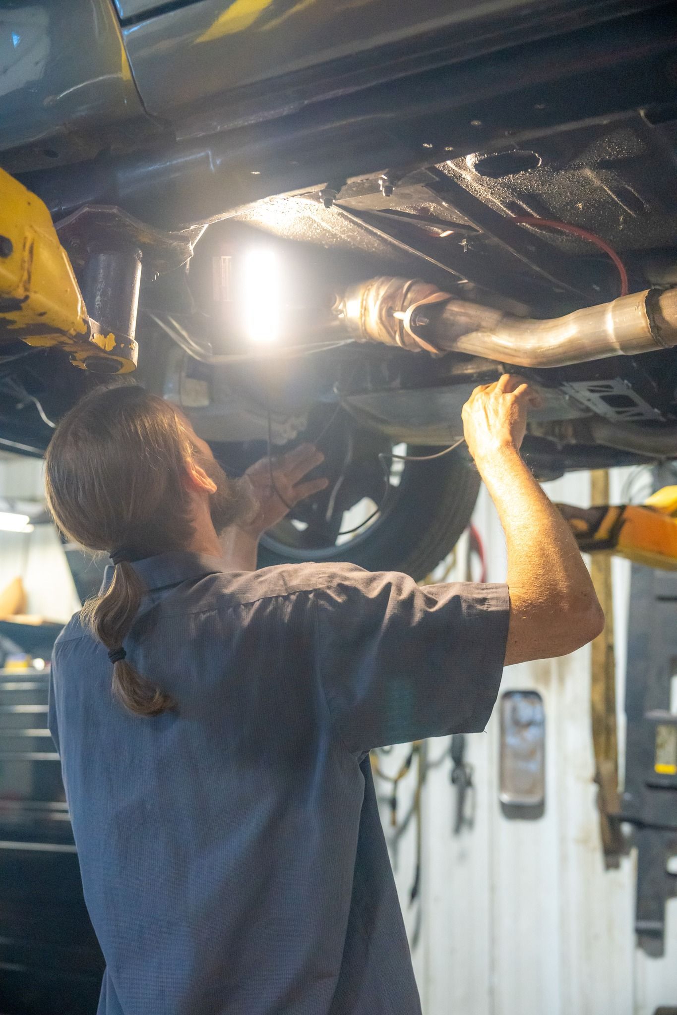 Mechanic working under a car, using a light, in a shop setting.
