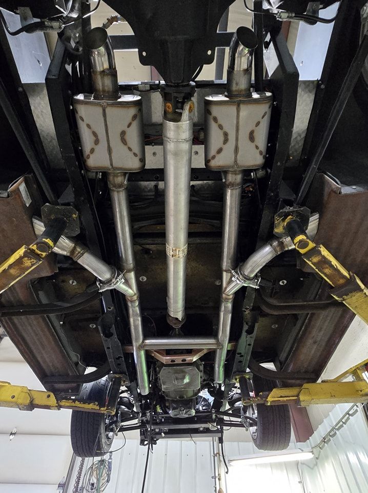 Undercarriage of a car with a custom stainless steel exhaust system, viewed from below.