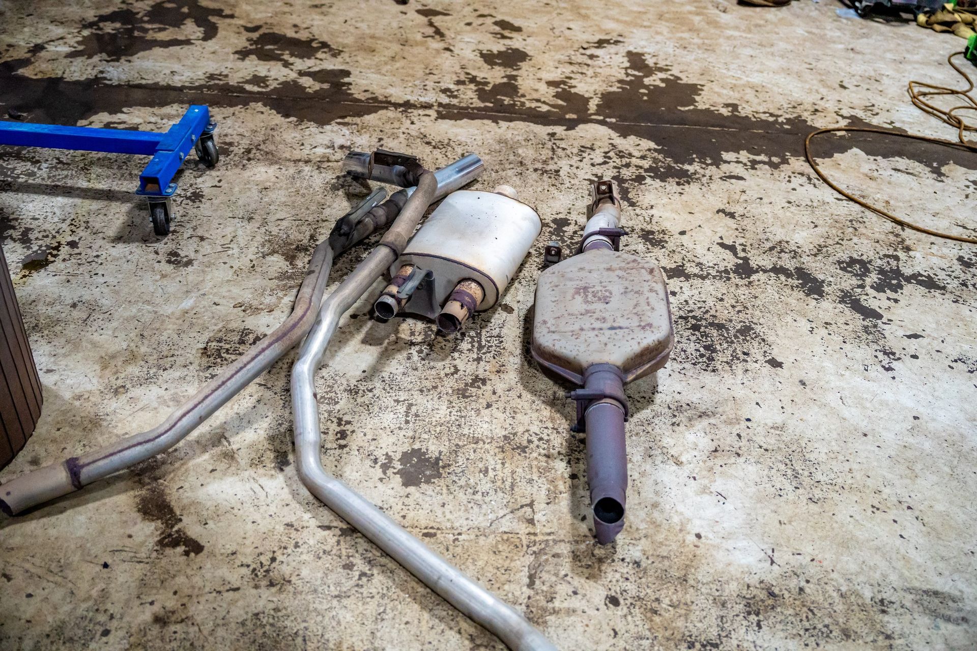 Car exhaust system components on a garage floor: pipes, mufflers, and catalytic converter.