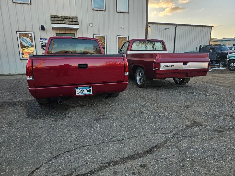Two red pickup trucks parked on asphalt in front of a building.