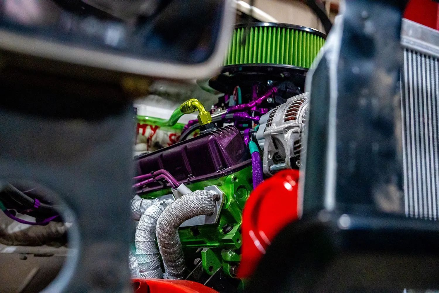 Green and purple engine, viewed through a car frame. Air filter, headers, and accessories.