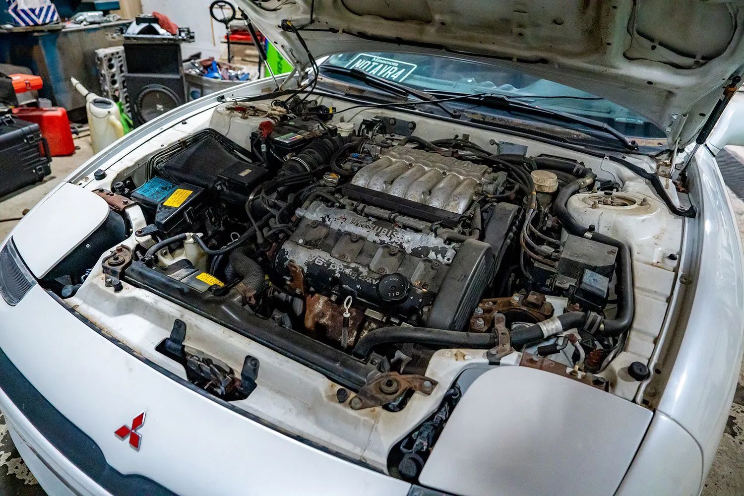 White car engine bay with the hood open, showing a dirty engine.