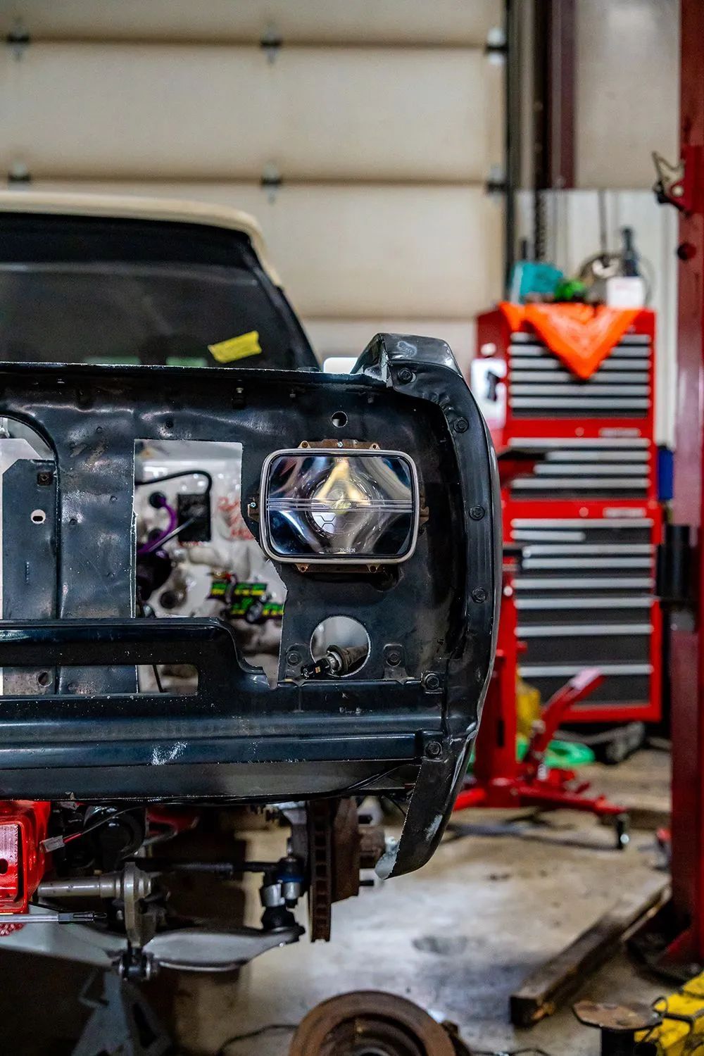 A classic car's front end undergoing restoration in a garage, featuring a headlight, tools, and a red lift.