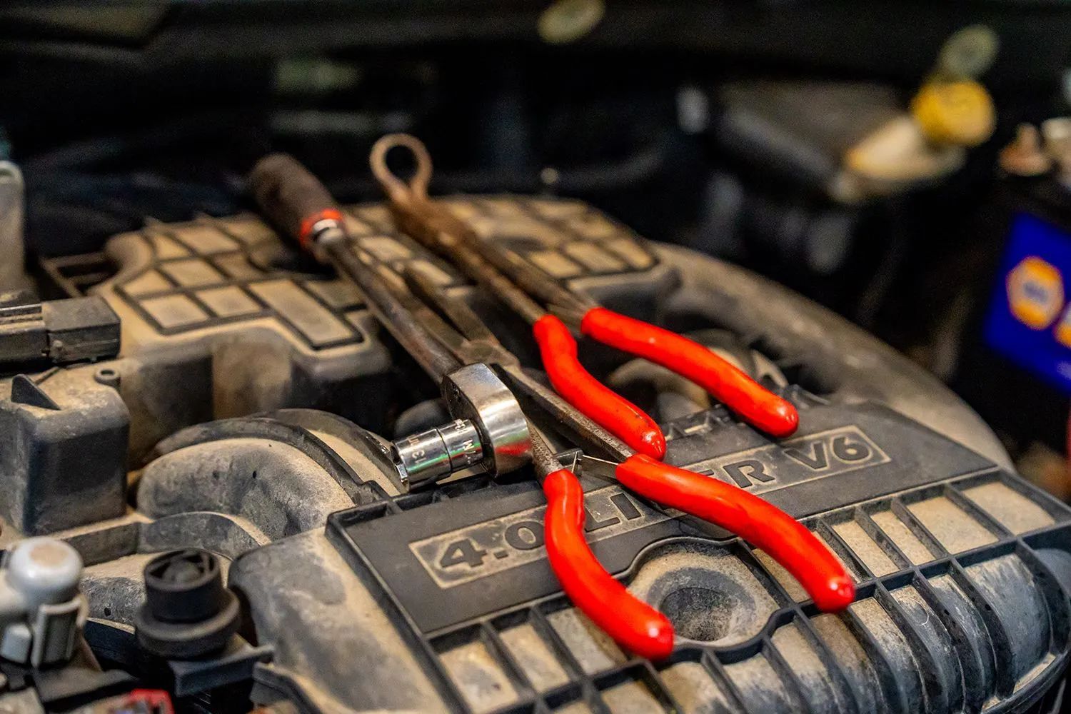 Tools with red handles on a dusty engine block: ratchet, pliers, and wrench.