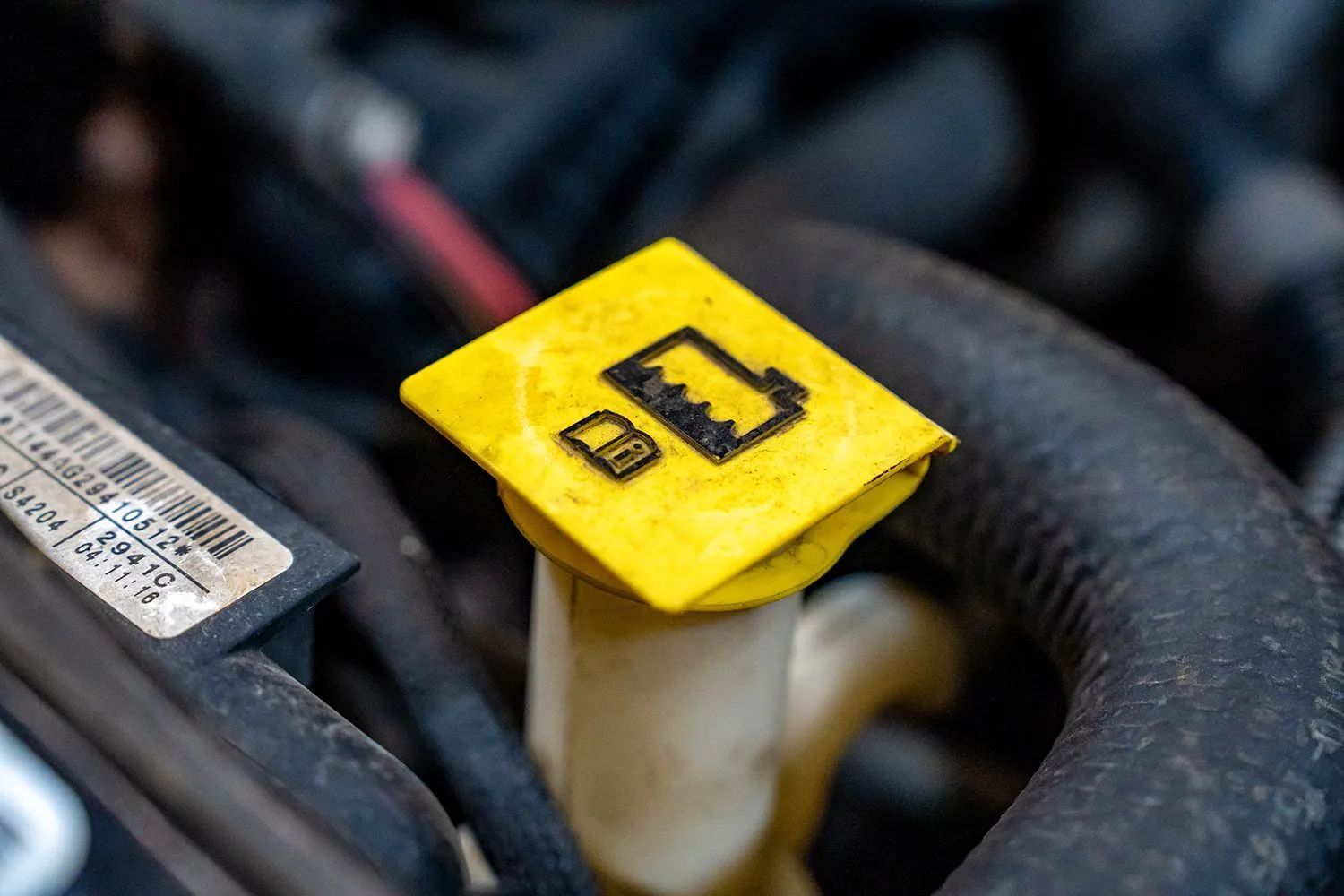 Yellow cap on a car's fluid reservoir, with windshield washer symbol.