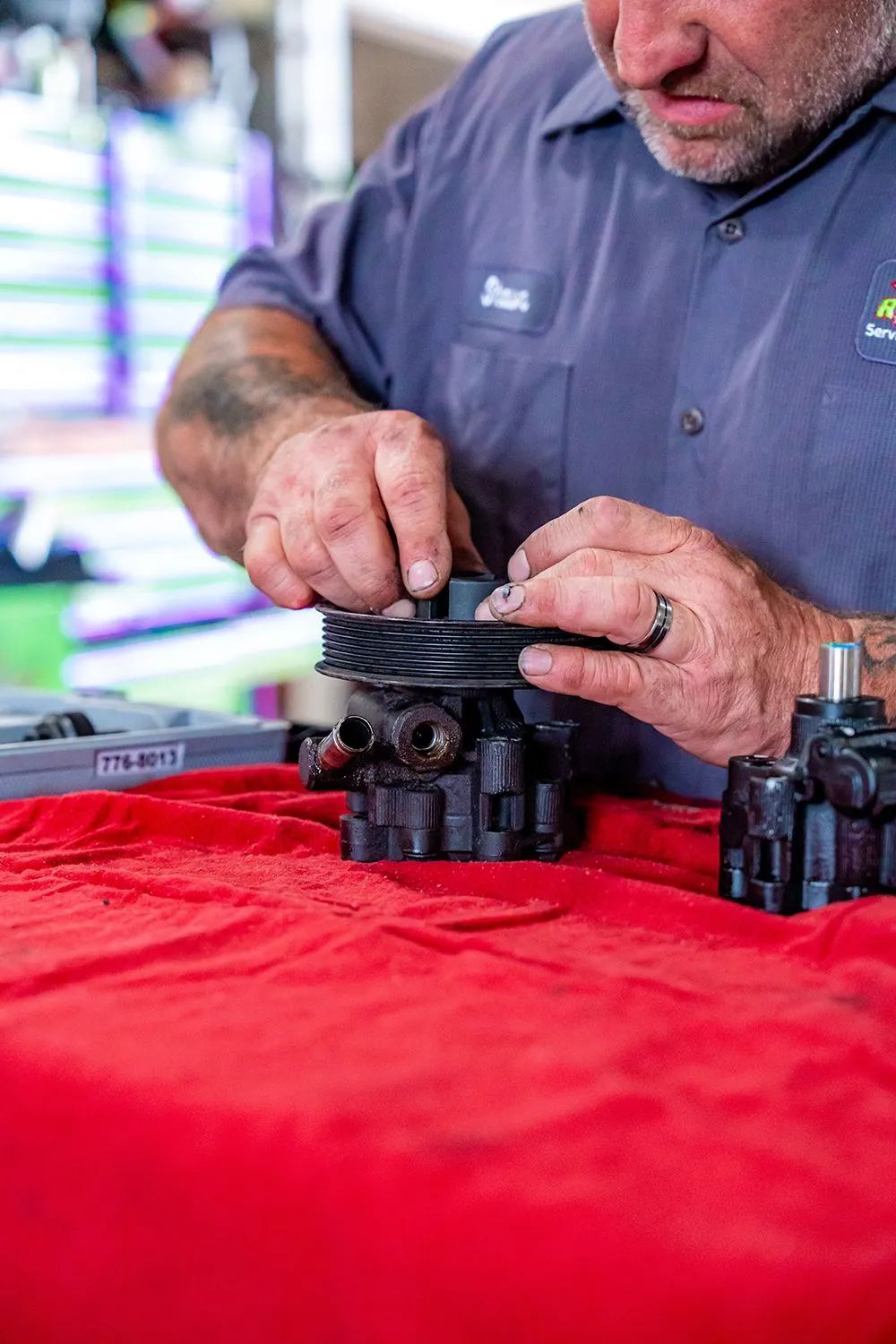 Mechanic in blue shirt working on a black car part on a red cloth.