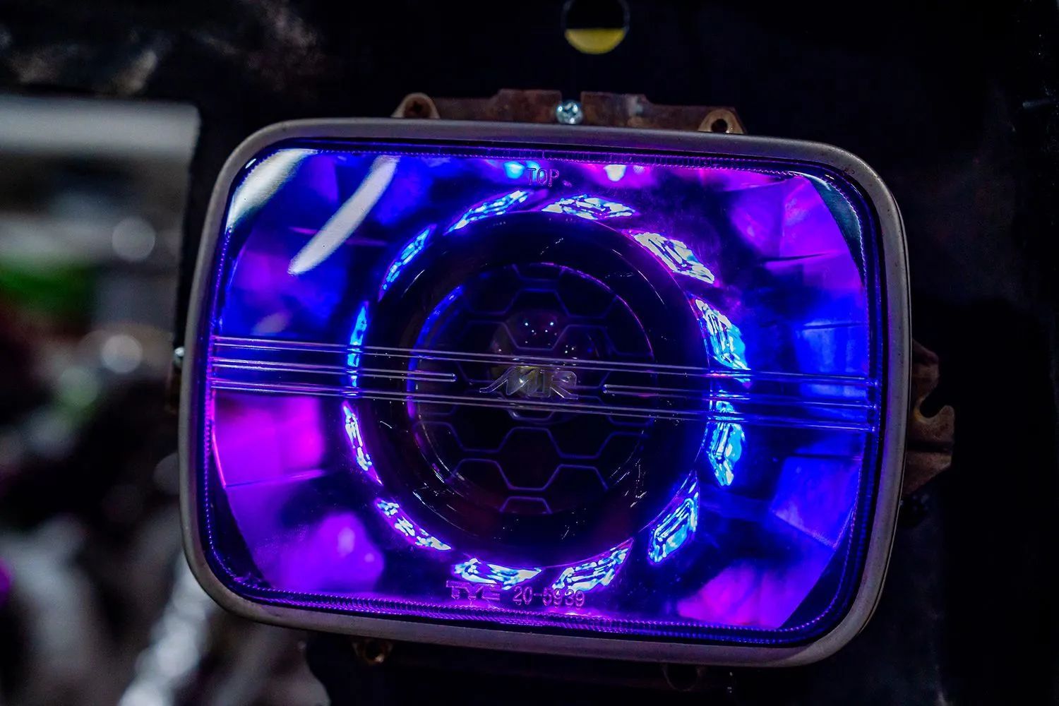 Purple-lit rectangular headlight with concentric circular patterns and a geometric center.