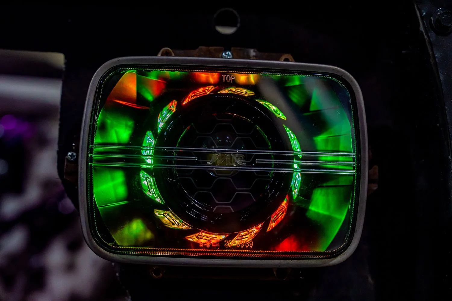 Square LED headlight with colorful green and orange swirling light patterns.