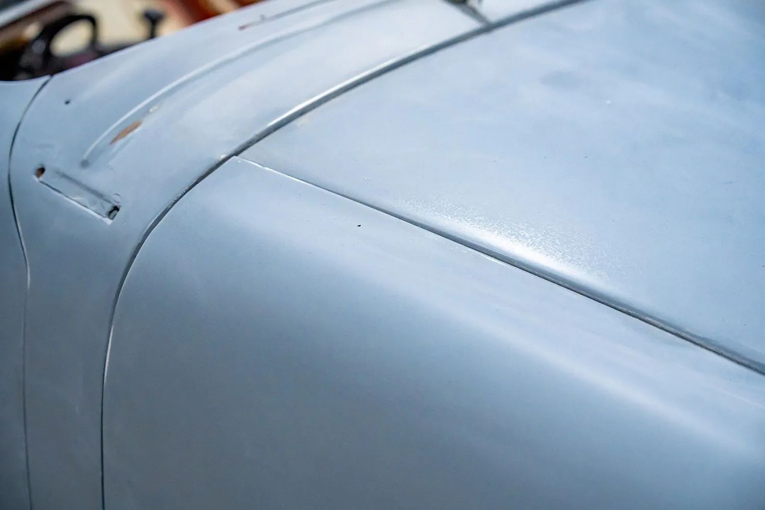 Close-up of a light blue car hood with a small metal strip along the top, exterior view.
