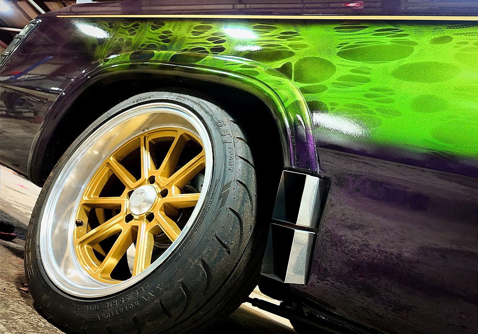 Gold-rimmed tire on custom purple car with green airbrush design.