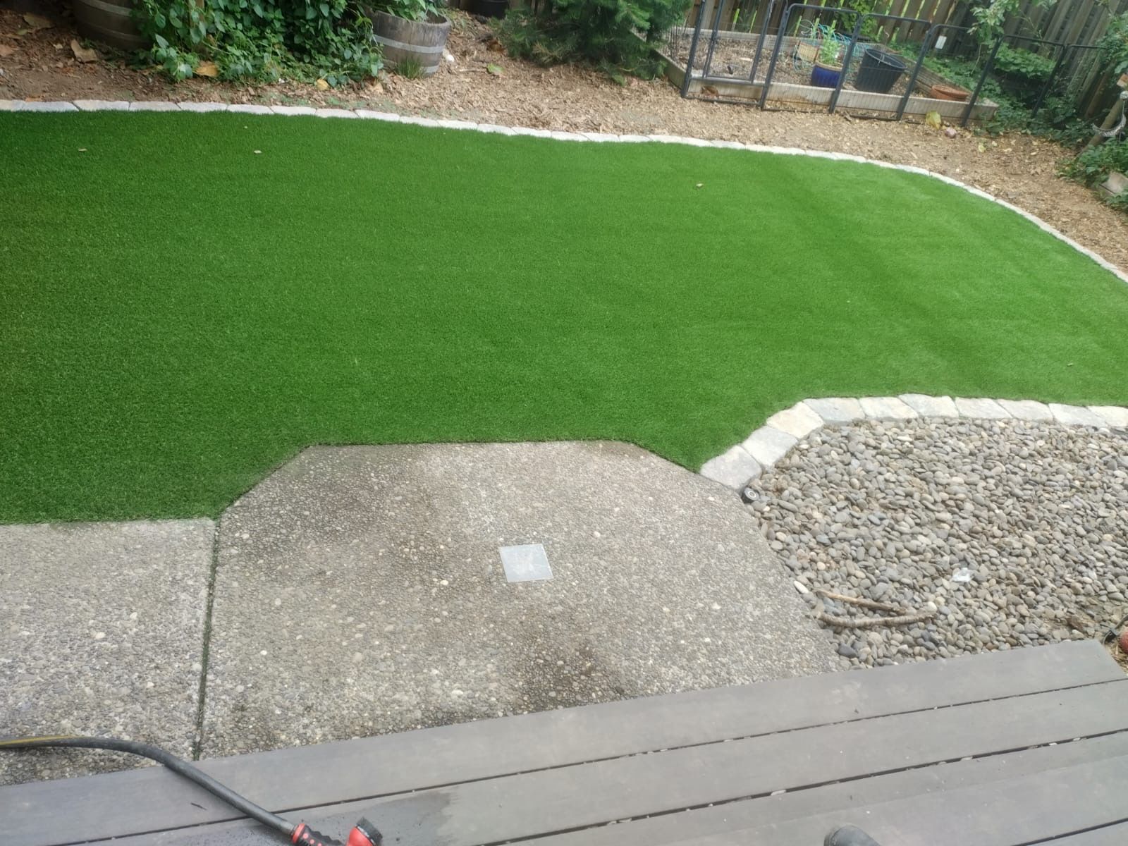 Green artificial turf lawn bordered by gravel and concrete steps.
