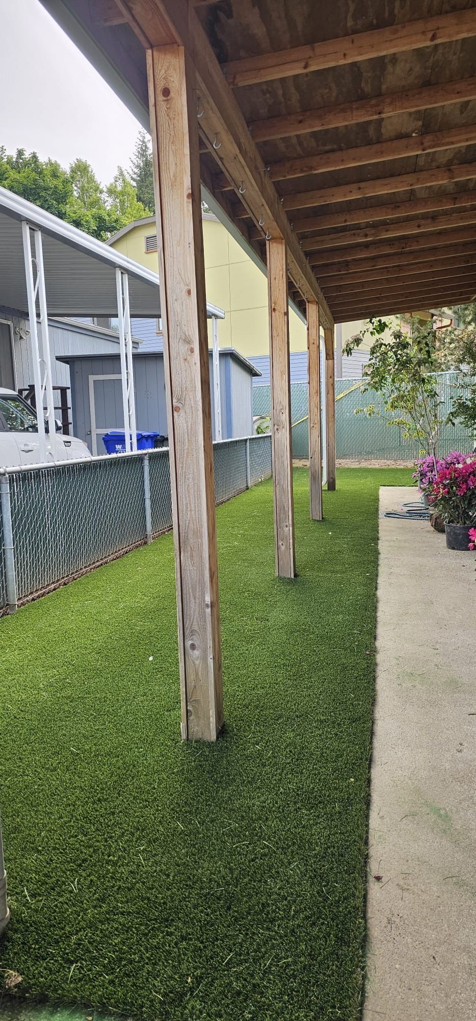 Wooden porch with columns next to a grassy lawn and fence.