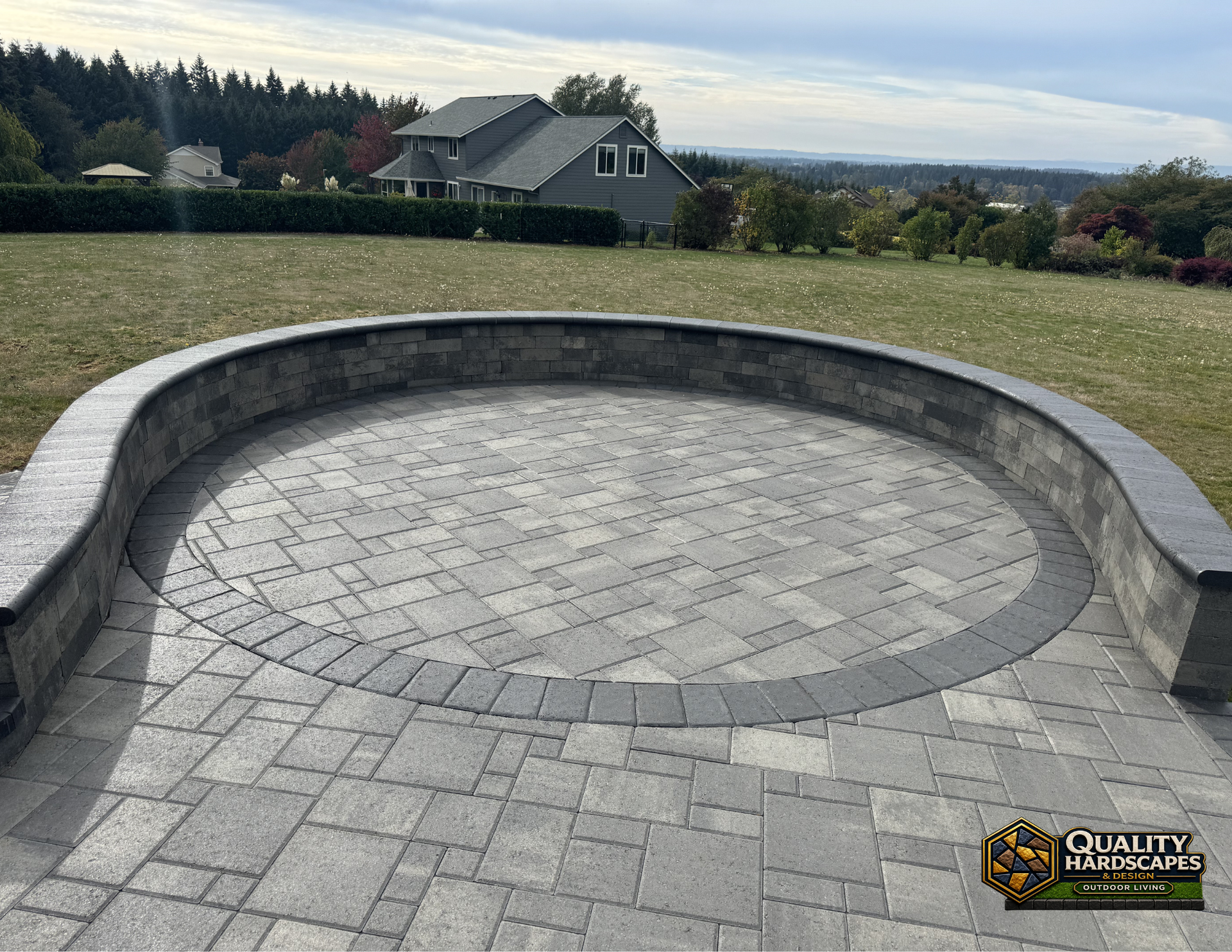 Curved stone patio with a circular fire pit border overlooking a grassy yard and distant trees