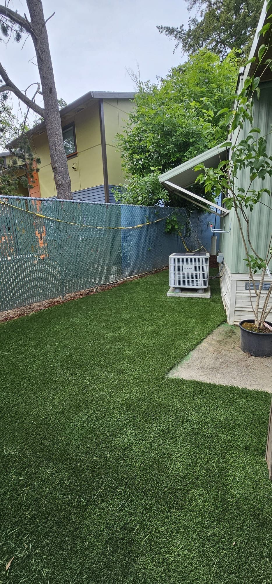 A small backyard with artificial turf, a chain-link fence, and a building on the right.