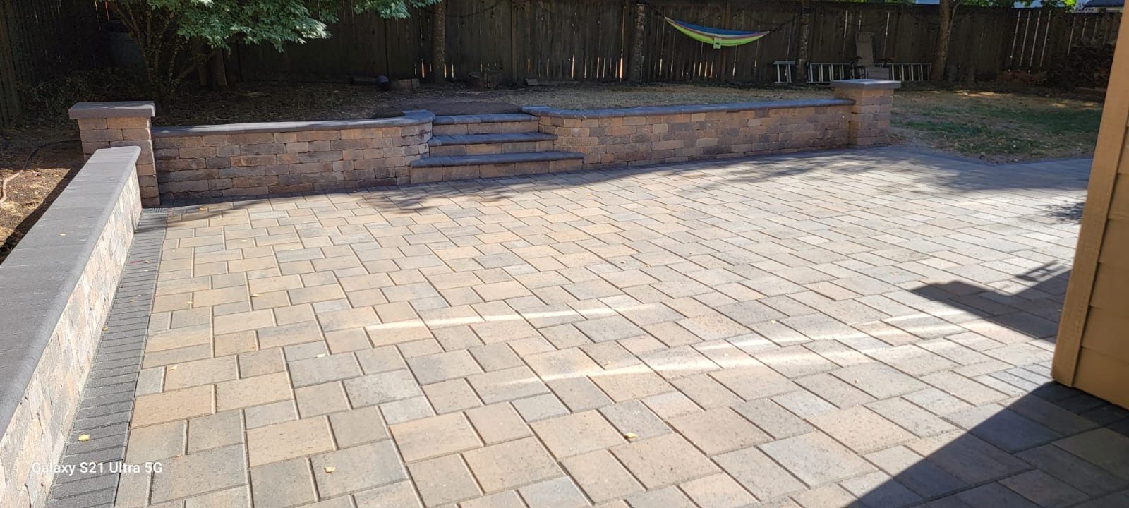 A brick patio with a raised stone wall, steps, and a wooden fence in the background.