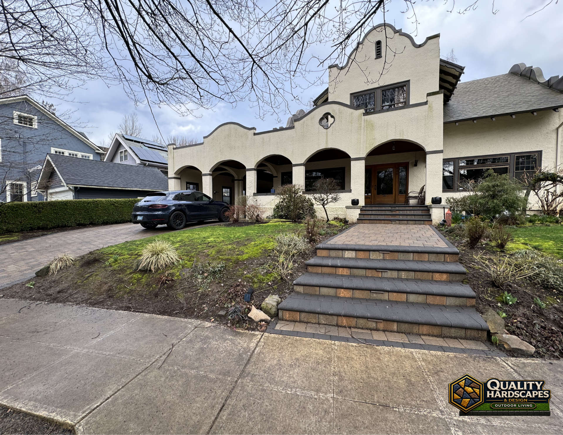 Stone-front house with arched porch, front steps, and a black car parked in the driveway.