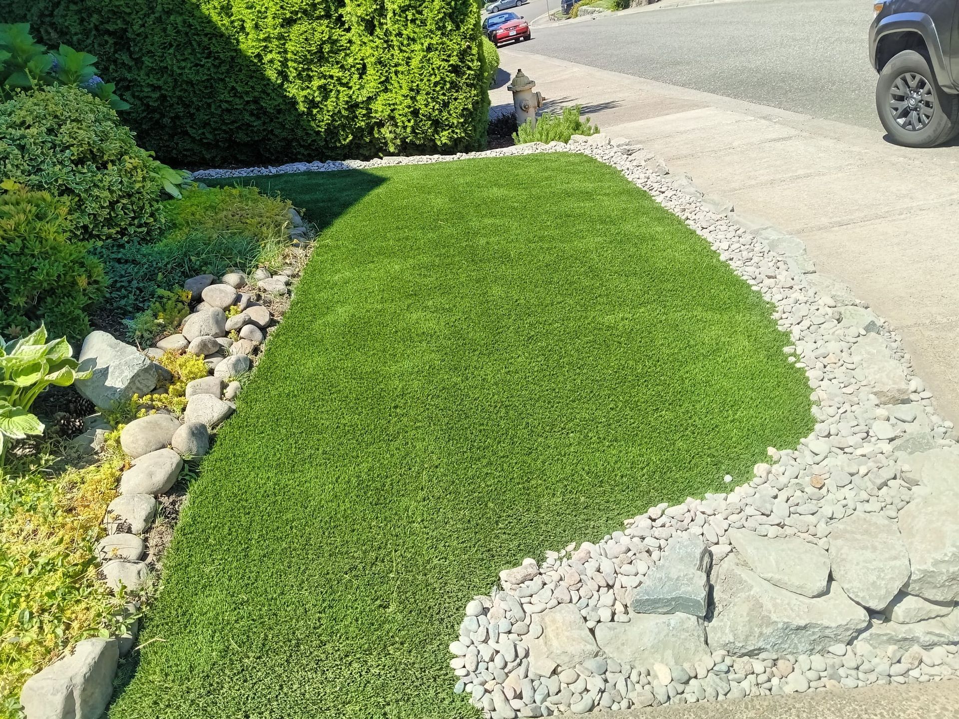 Lush green lawn edged with rocks, adjacent to a sidewalk and planted shrubs.