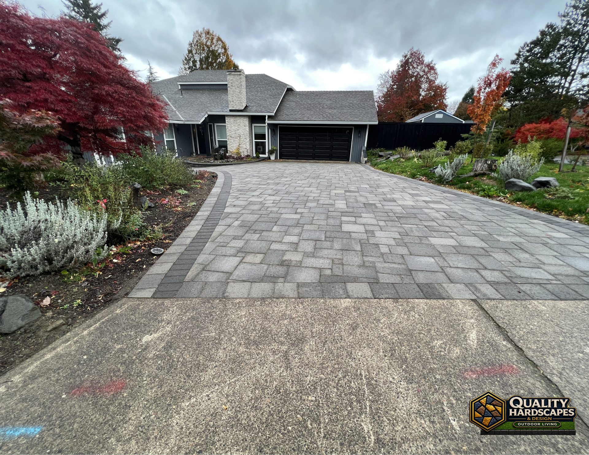 Residential driveway leading to a stone house with autumn landscaping and a black garage door