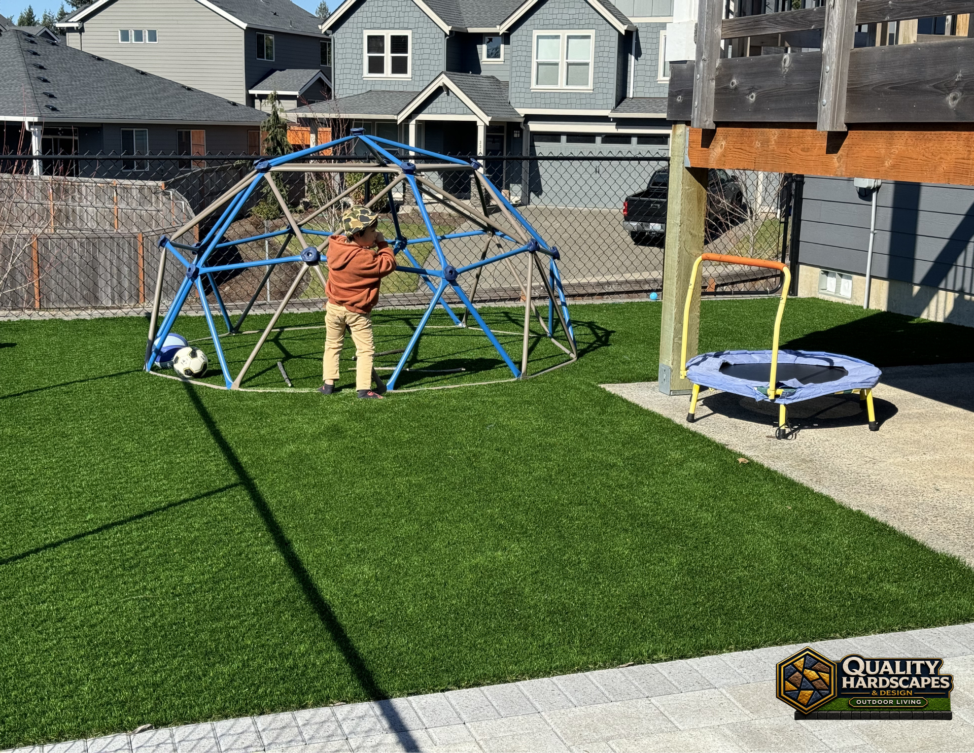Child climbing a blue geodesic dome in a backyard with a trampoline and houses in the background