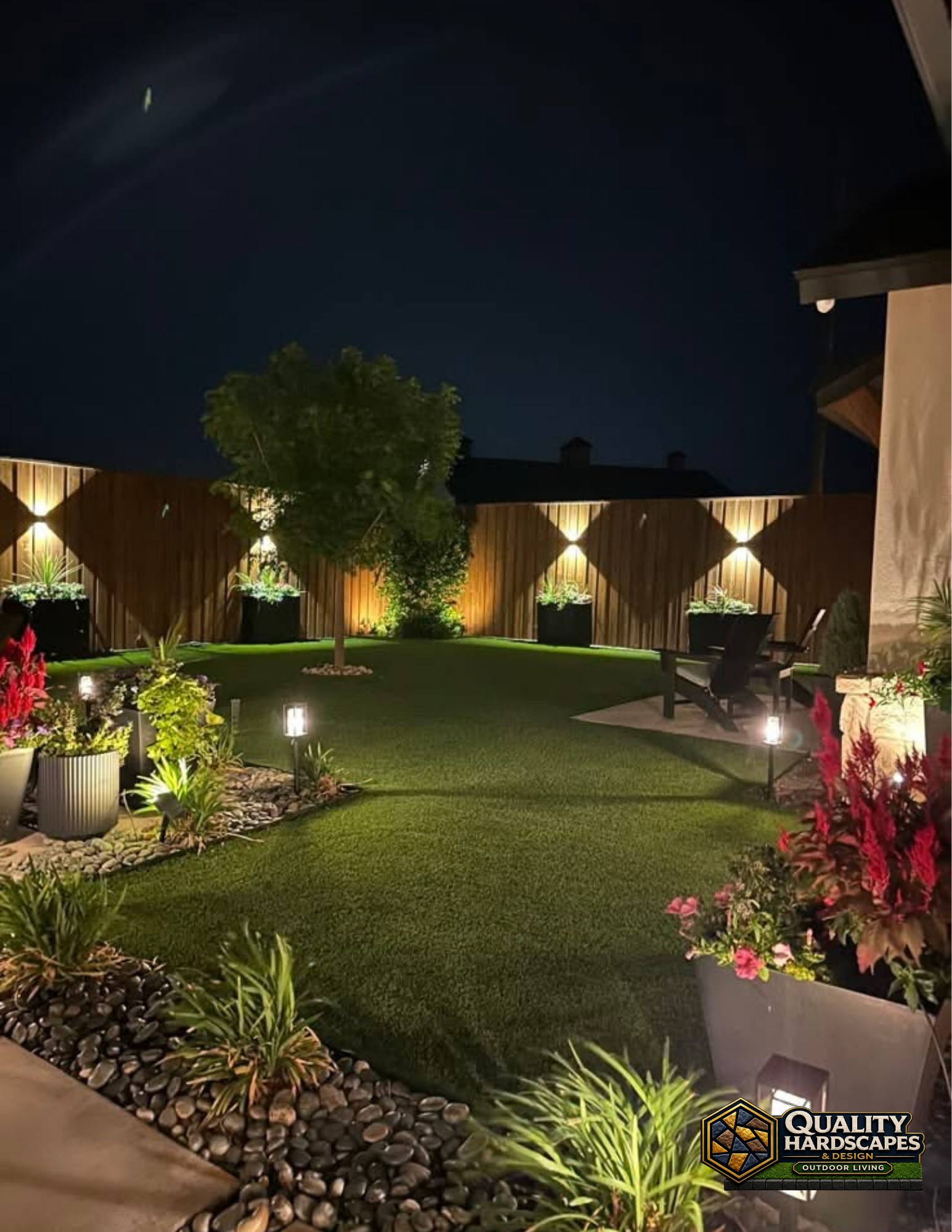 Illuminated backyard garden with trimmed lawn, flower beds, and warm fence lights at night