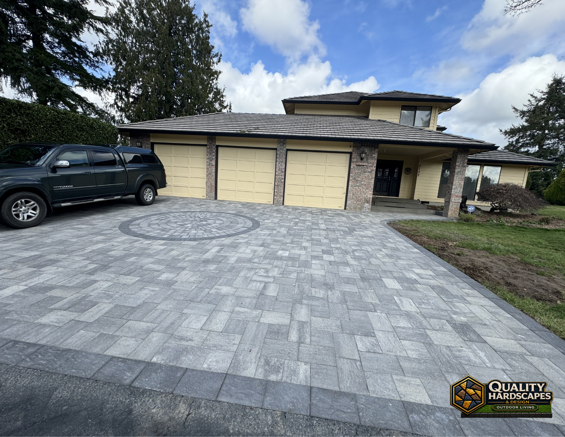 Stone-paved driveway leading to a beige two-car garage with a black SUV parked on the left.