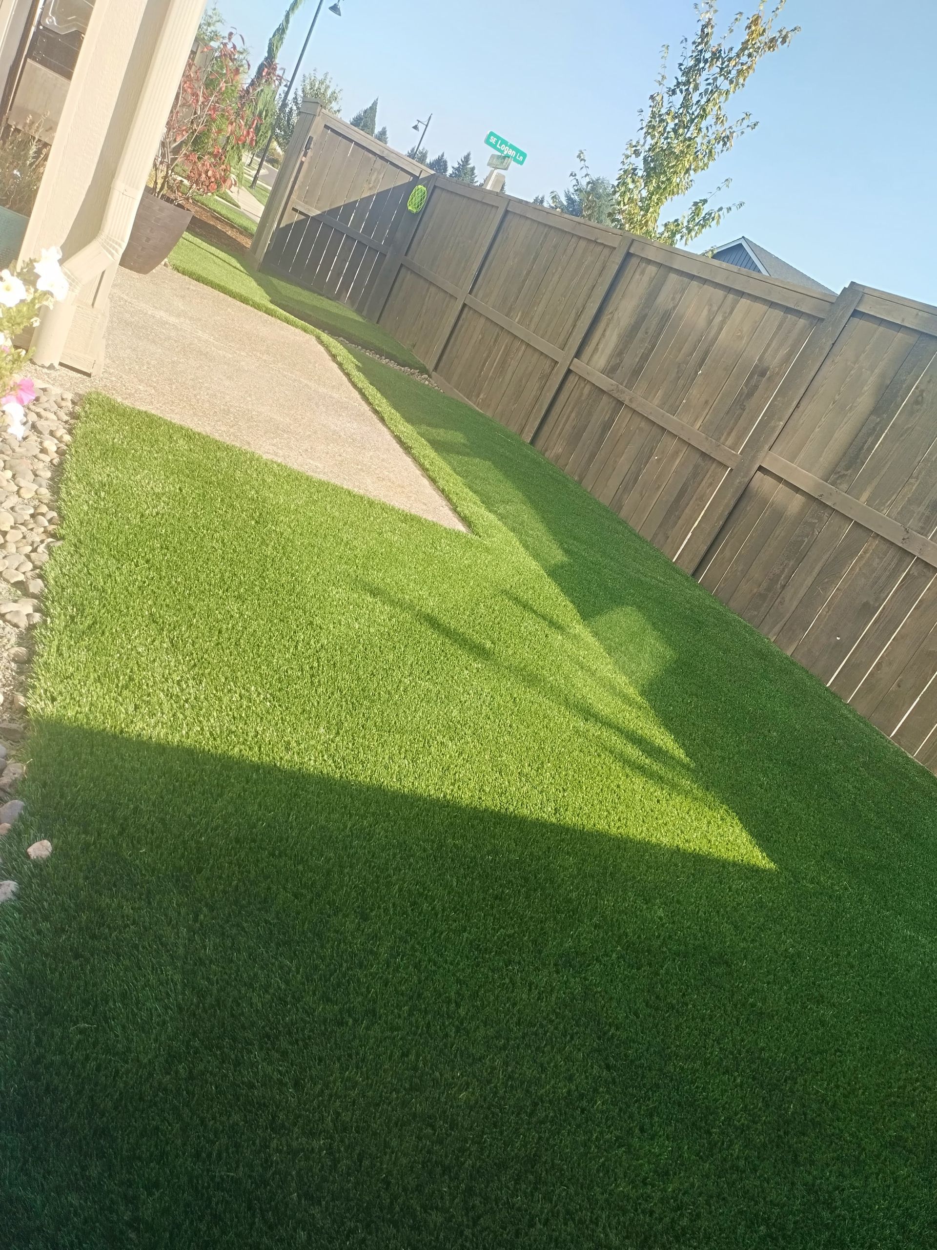 Green artificial turf lawn next to a wooden fence and concrete patio on a sunny day.
