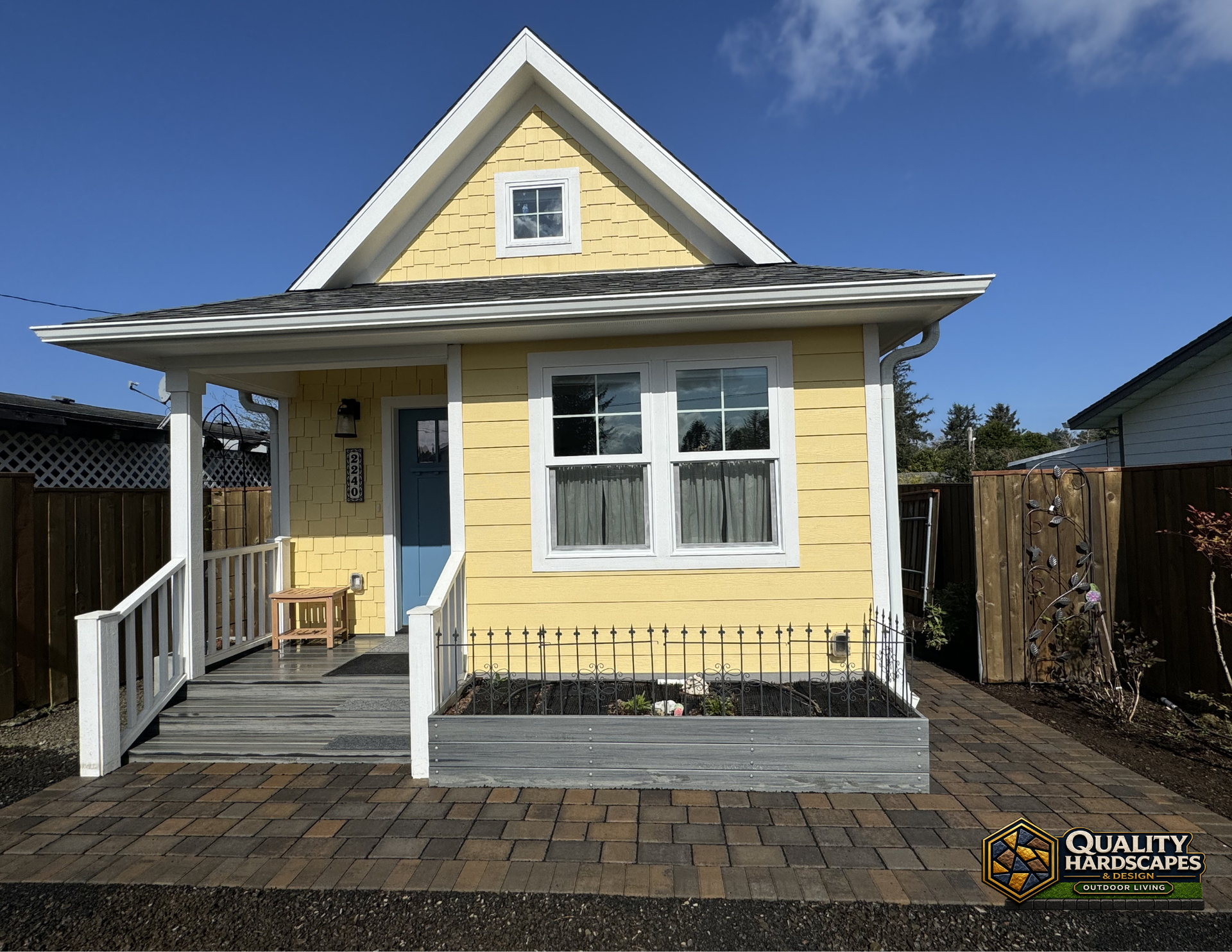 Small yellow bungalow with white trim, front porch, and fenced yard on a sunny day