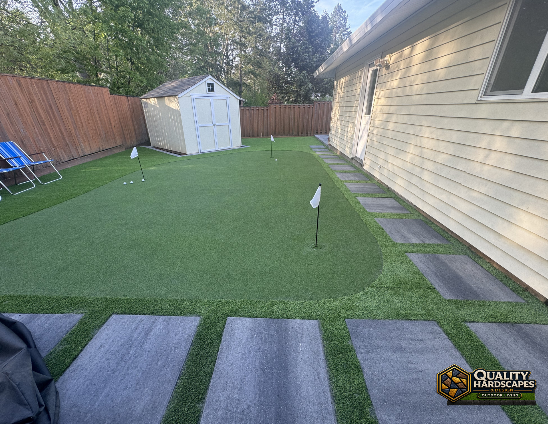 Backyard with artificial turf, stone path, fence, shed, and a house wall on the right.