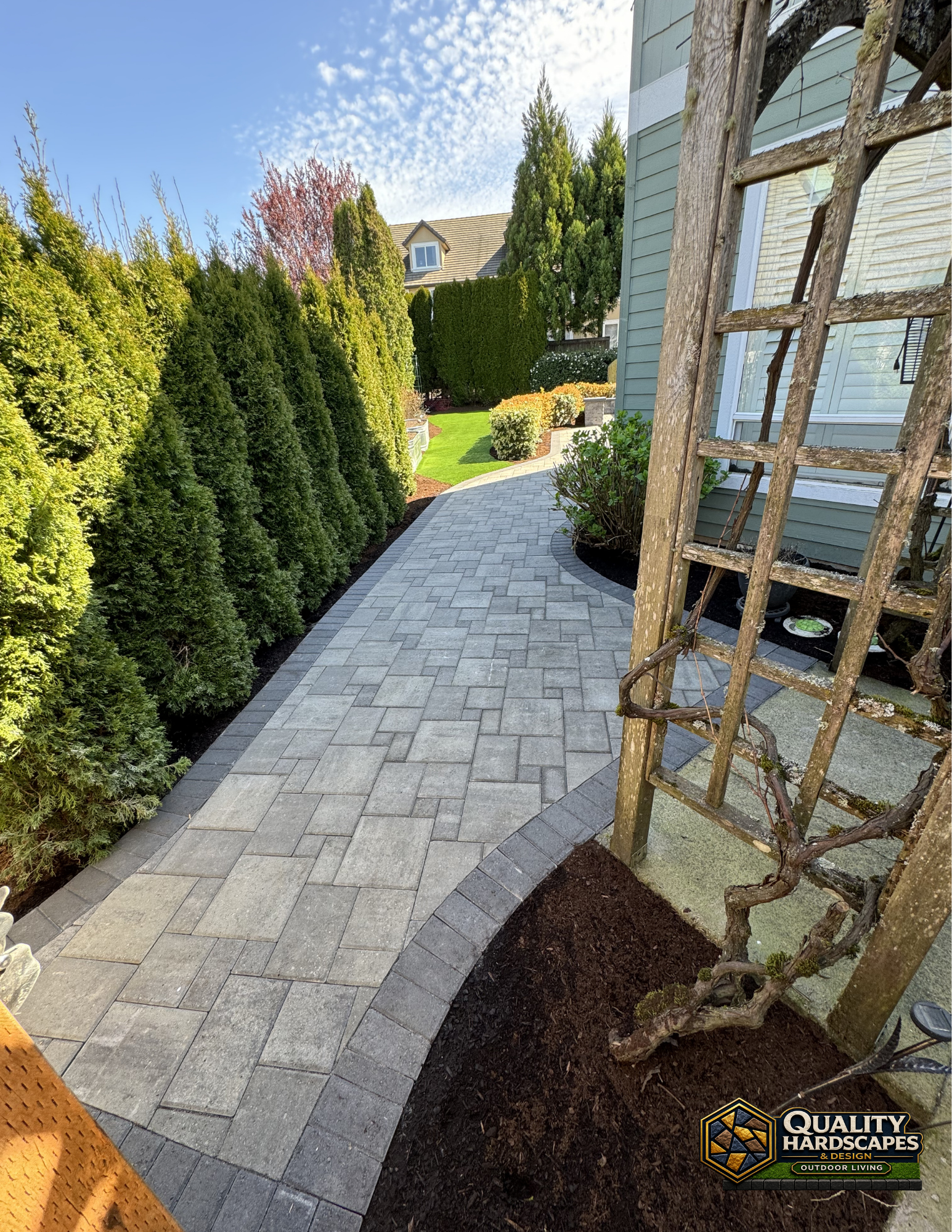 Curved stone walkway beside tall green hedges and a landscaped garden