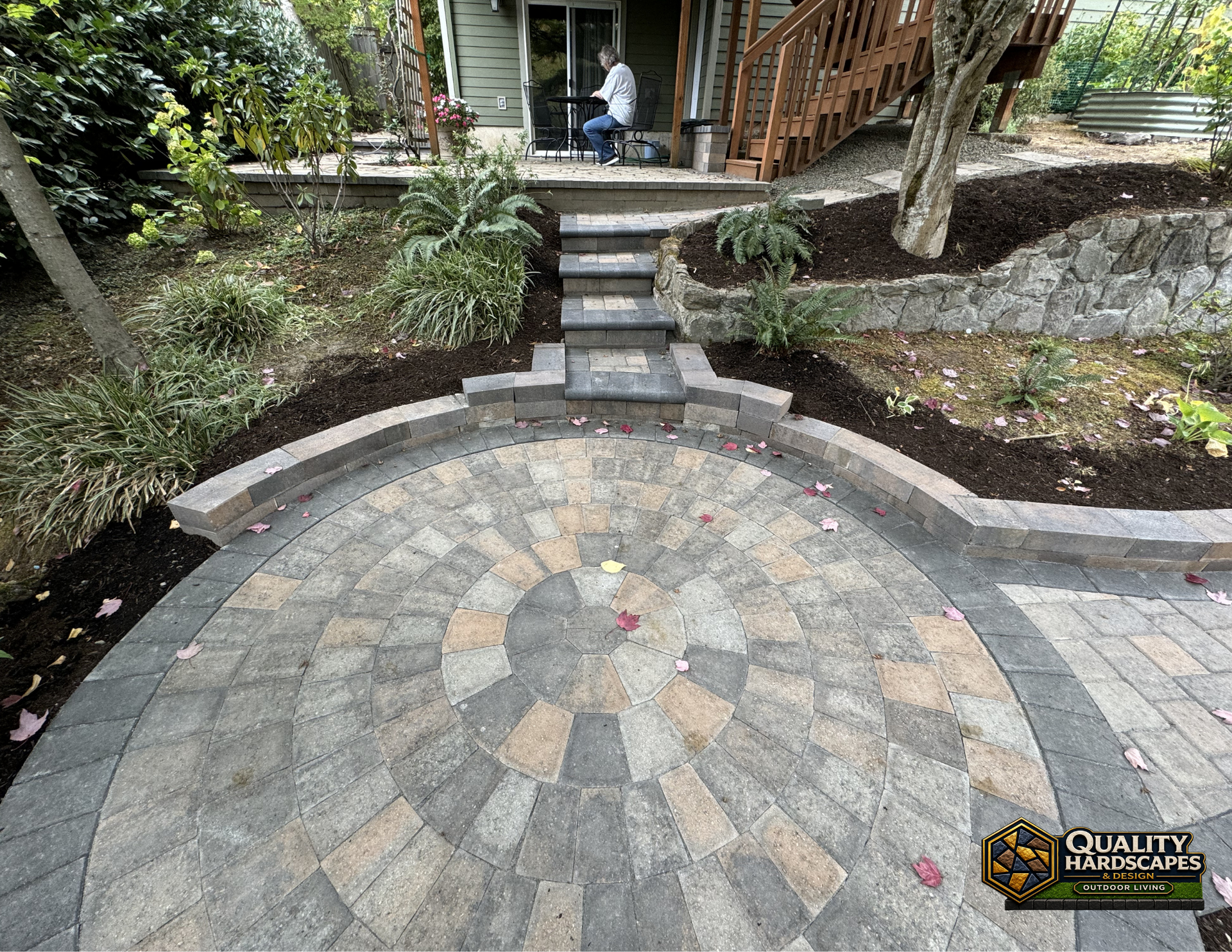 Circular stone patio with curved steps leading to a raised deck and landscaped garden borders