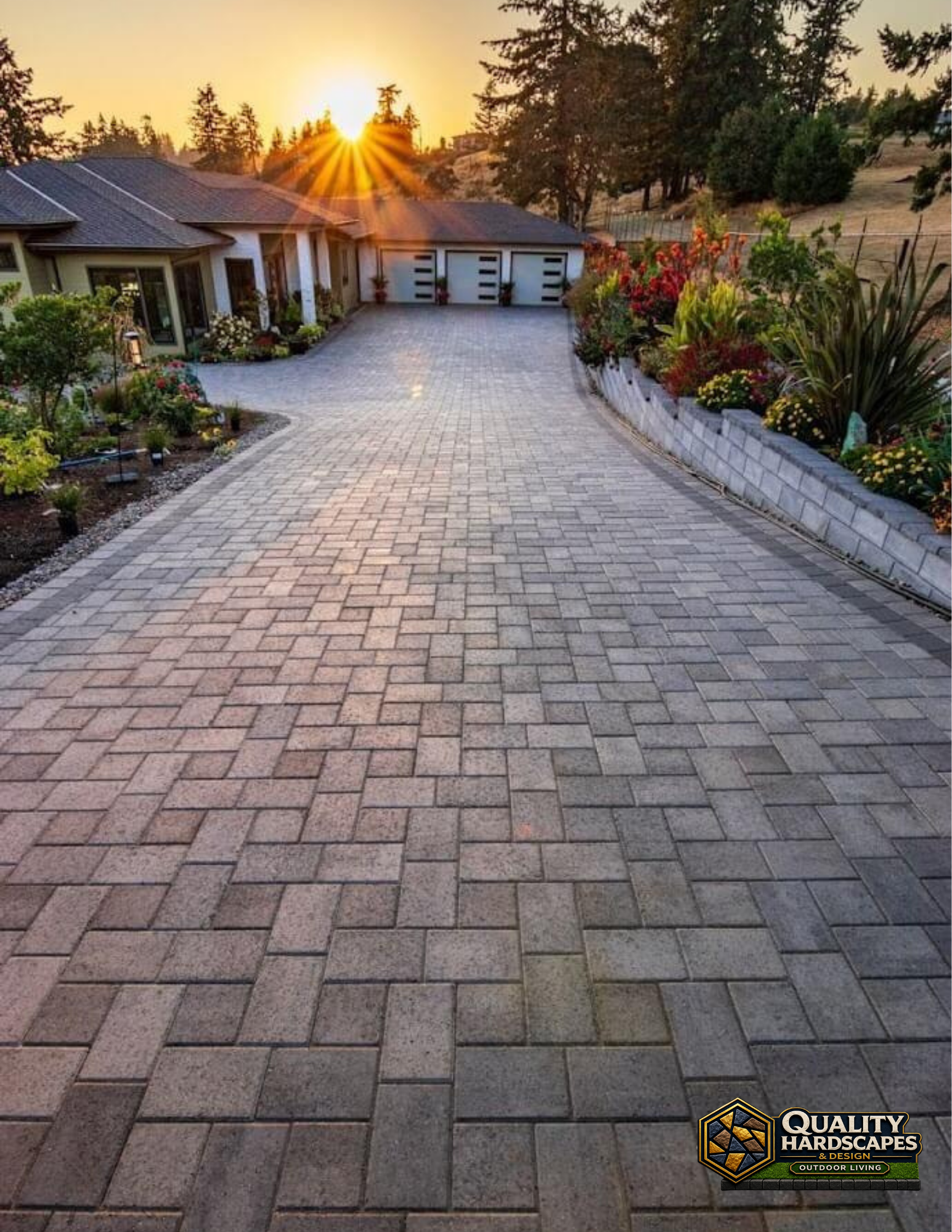 Brick-paver driveway leading to a house at sunset, with landscaped flower beds on both sides