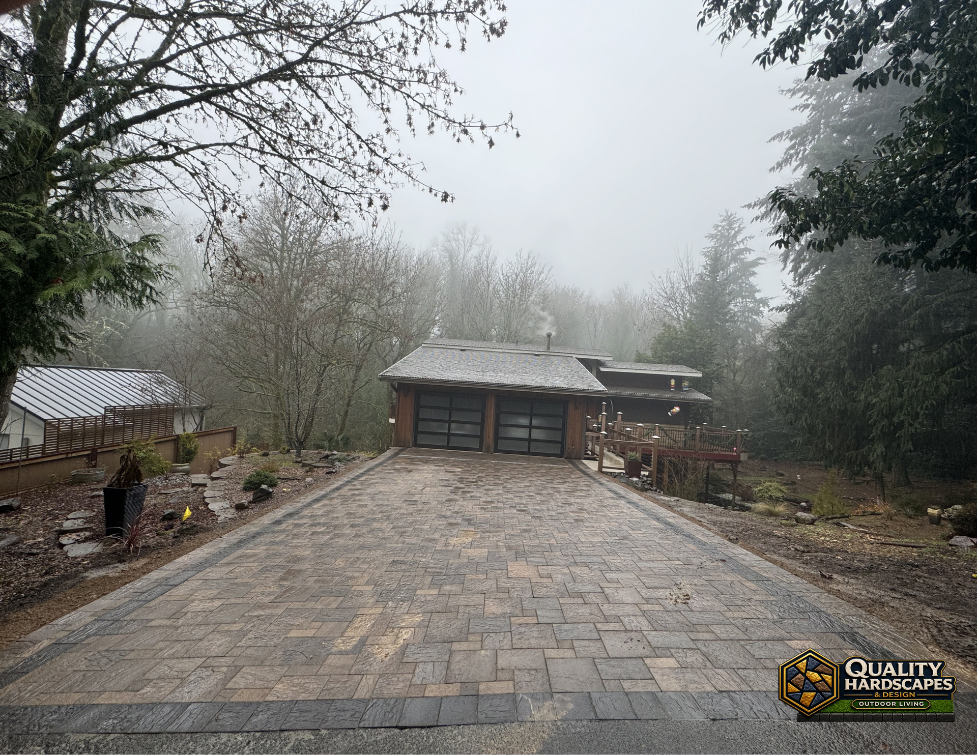 Foggy driveway leading to a small garage and house, with trees and garden beds on both sides.